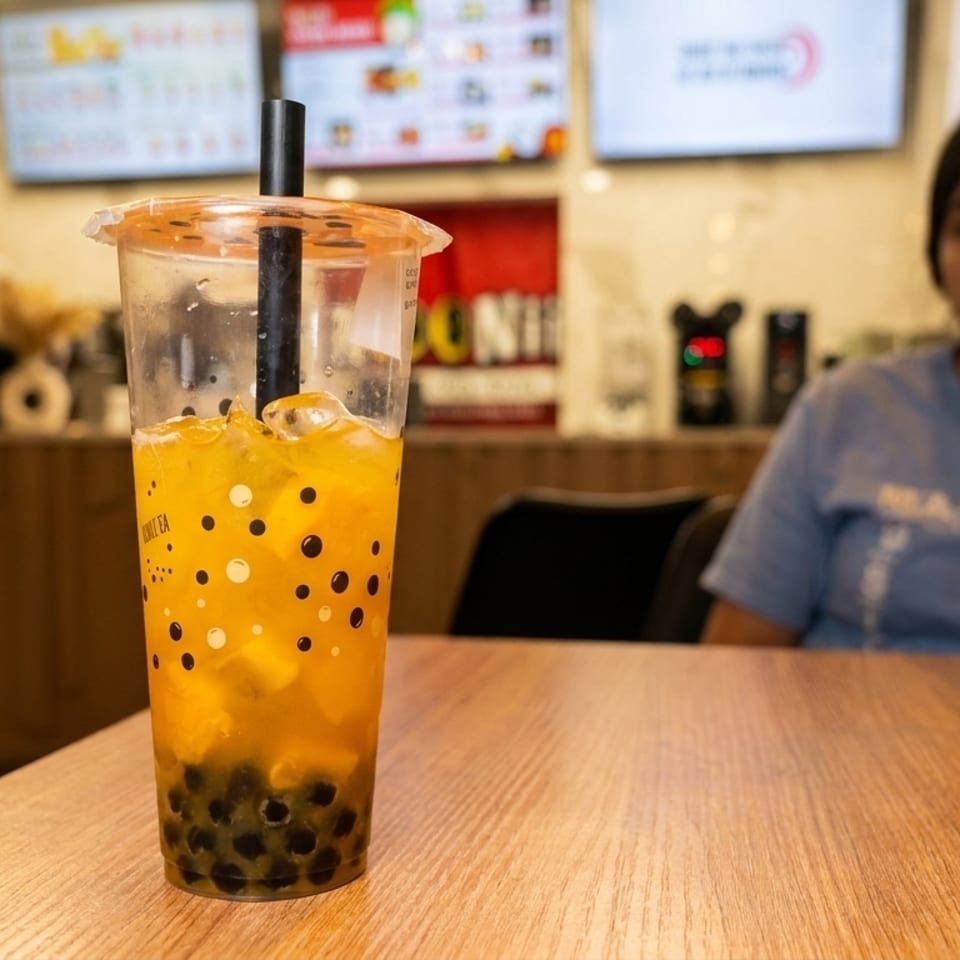 A mango boba tea with black tapioca pearls on a wooden table, with a person in the background.