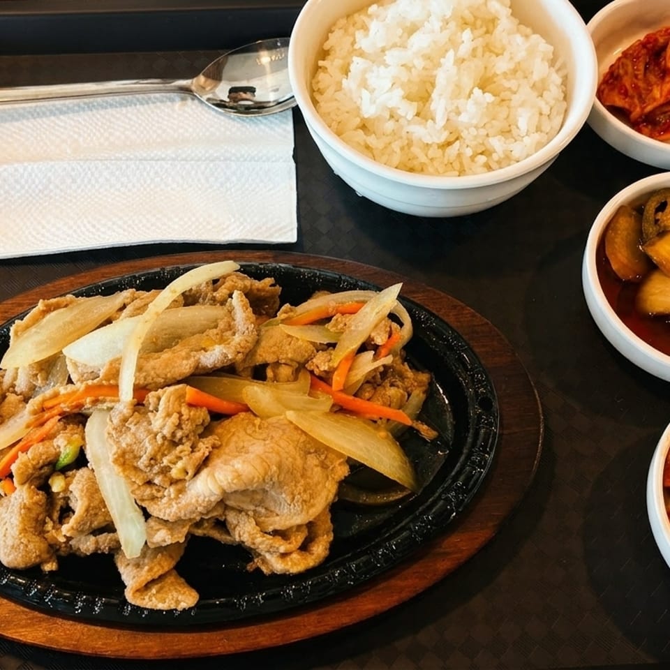 Korean BBQ pork with onions and carrots, rice, and three side dishes on a black tray.