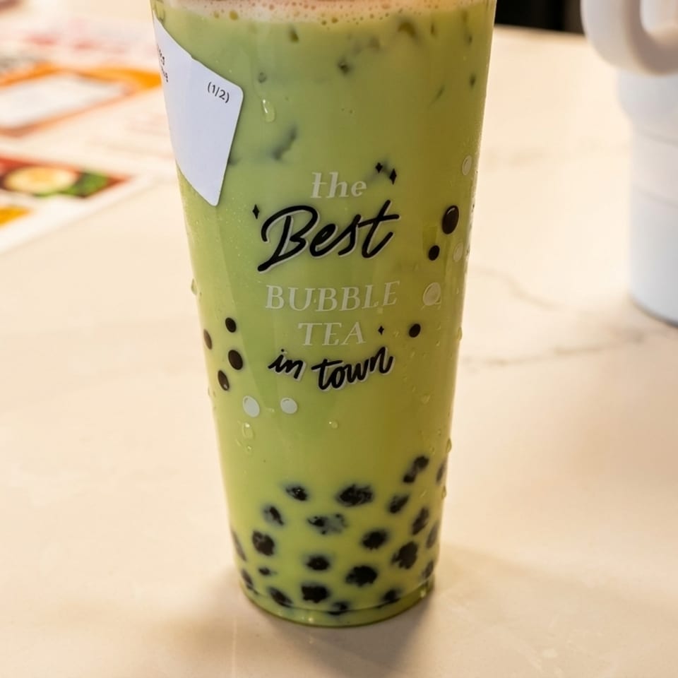 Green bubble tea with tapioca pearls in a clear cup on a white counter with a menu.