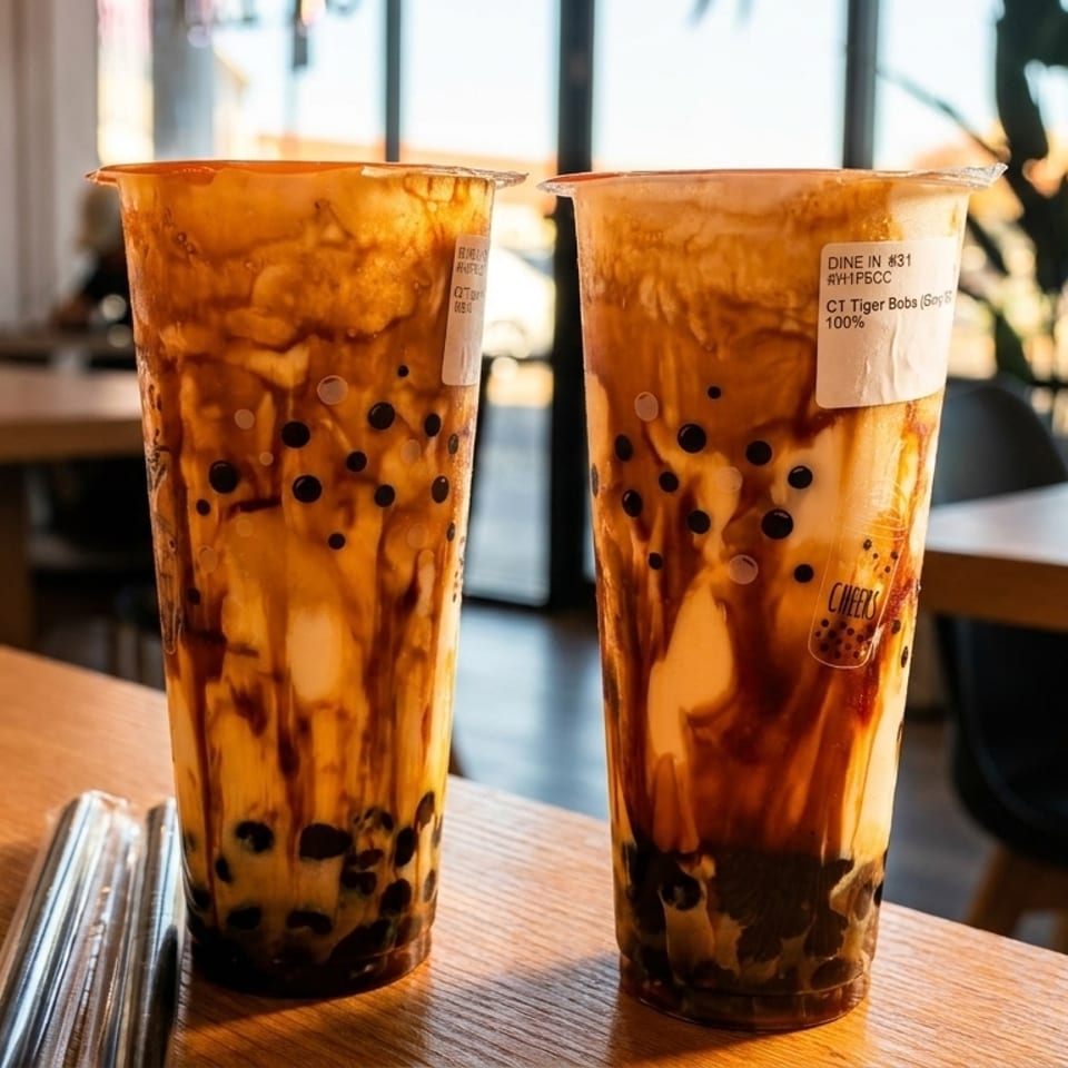 Two tall plastic cups of brown sugar boba tea with dark tapioca pearls on a wooden table.